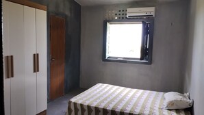 A bedroom with a bed, a wardrobe, a window, and an air conditioning unit. - Ap. André Ângelo (Sirinhaém)