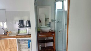 A compact hotel room with a kitchenette, a bathroom with a glass shower, and a bed. - Studio 1 Je Nous between the Sea and the Lagoon (Faro de José Ignacio , la Juanita)
