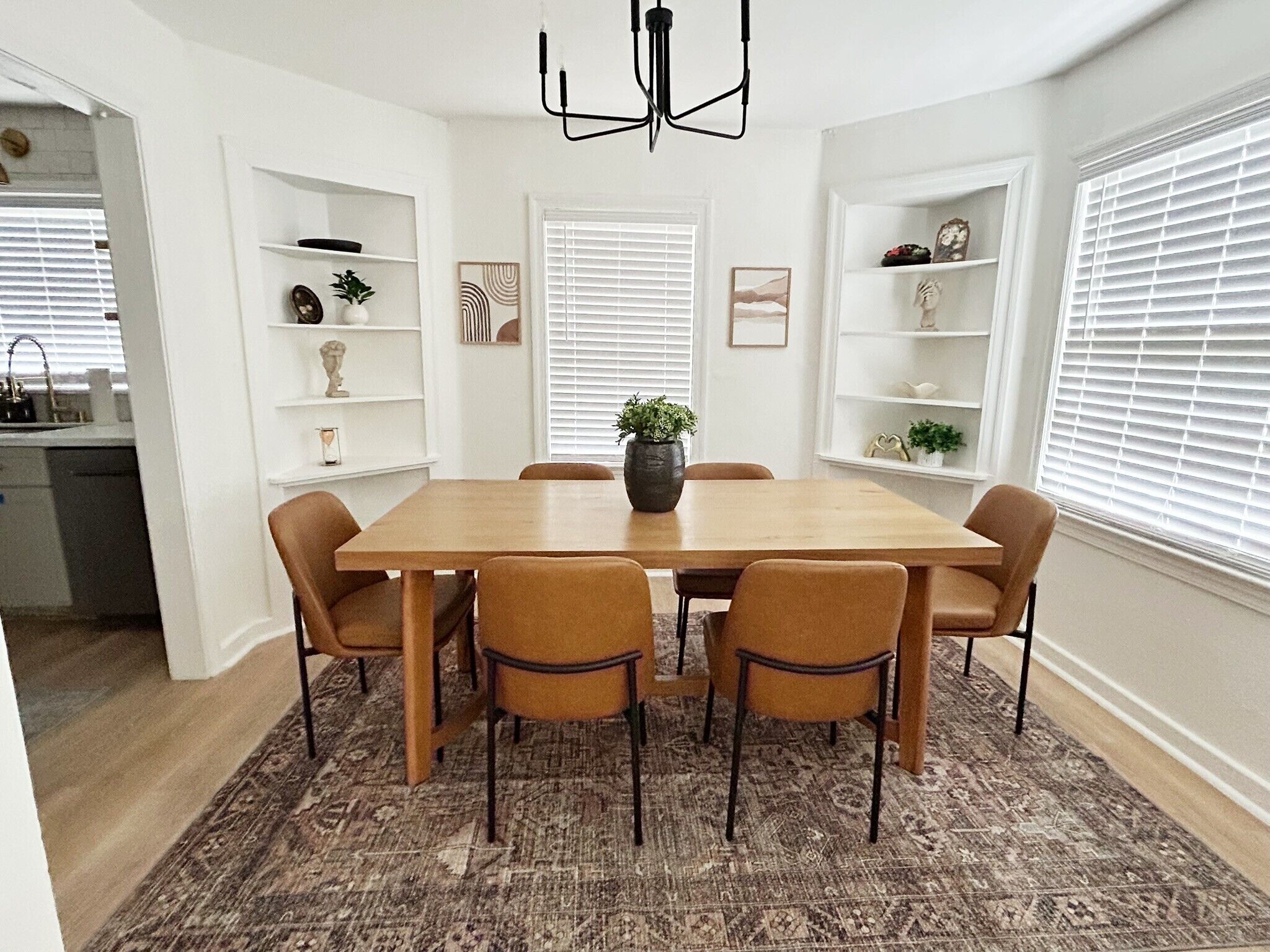 Une salle à manger avec une table en bois et six chaises, un lustre et un tapis à motifs.