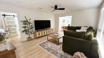 A modern living room with a green sofa, a flat-screen TV, a wooden coffee table, and a patterned rug.