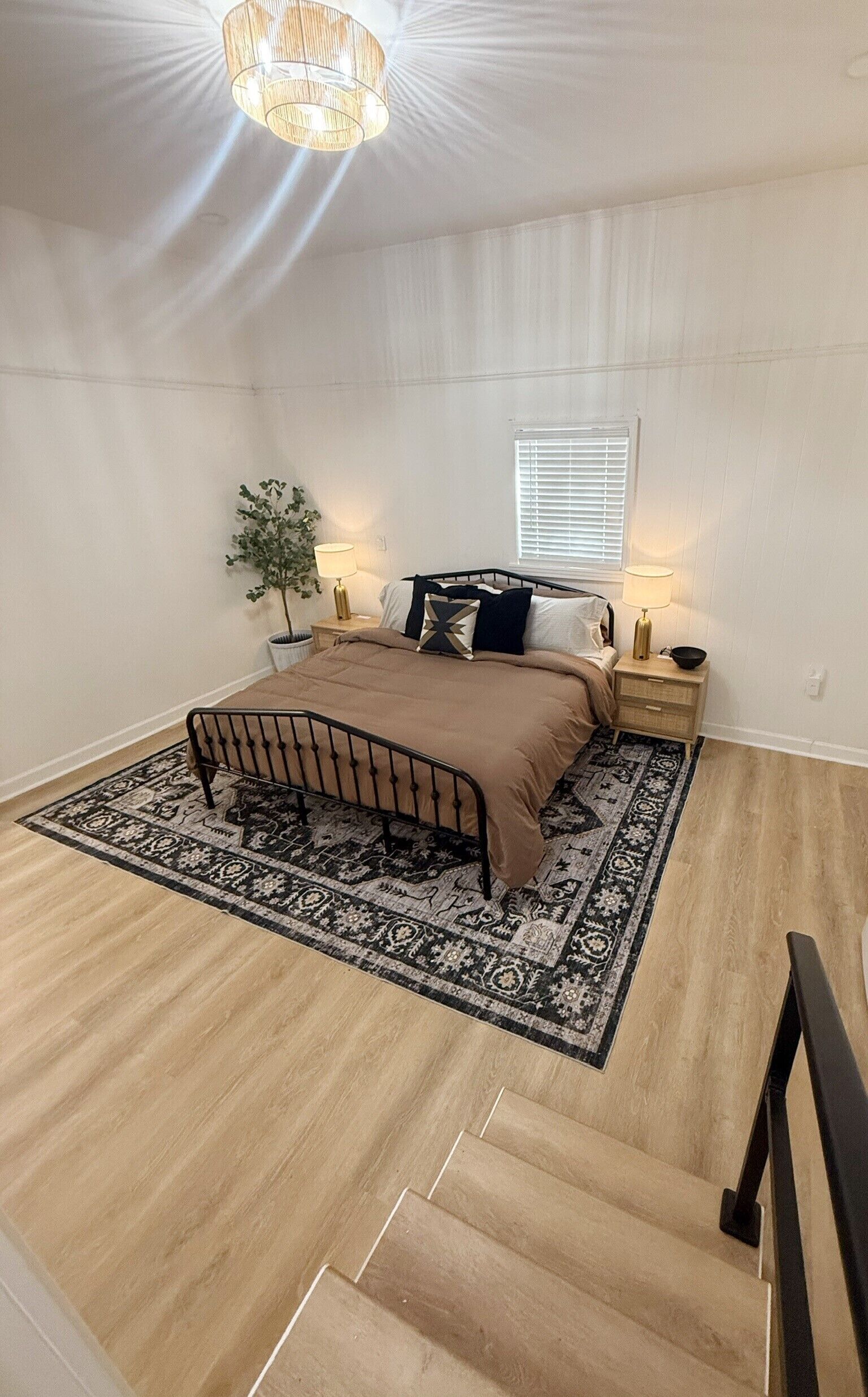 Une chambre à coucher avec un lit, des lampes de chevet, une fenêtre, une plante et un escalier.