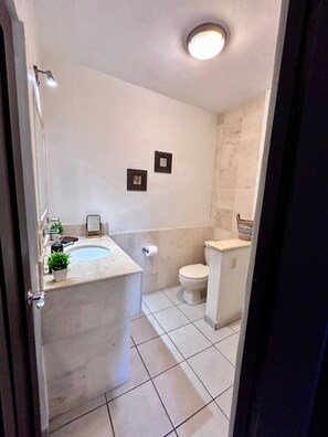 Een badkamer met een wit wastafel, toilet en een klein spiegel. Twee ingelijste foto's hangen aan de muur.