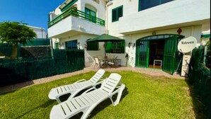 A two-story house with a balcony, a patio with a table and chairs, and a green lawn.