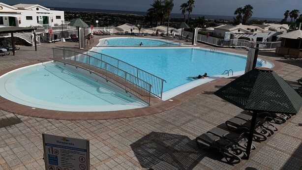 A large outdoor swimming pool with a surrounding deck, lounge chairs, and a covered seating area.