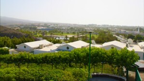 A residential area with white-roofed houses, green trees, and a clear sky.