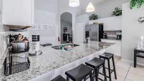 A modern kitchen with a granite countertop, stainless steel appliances, and bar stools. - Villa With Private Pool in Lake Berkley Resort (Kissimmee)