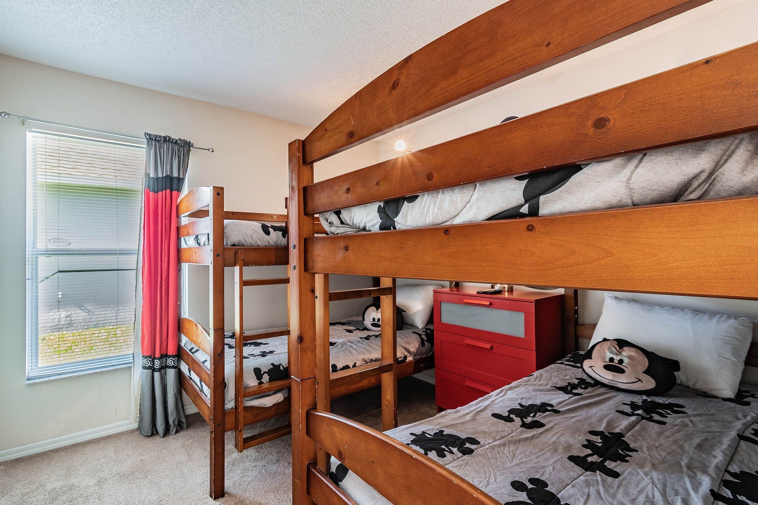 A bunk bed room with a window, curtains, and a red dresser.