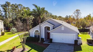 A single-story house with a garage, a front yard with a lawn and a tree, and a driveway leading to the garage. - Villa With Private Pool in Lake Berkley Resort (Kissimmee)