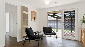 A room with two black chairs, a small table, a white door, a vent, a framed artwork, and a sliding glass door leading outside. - Family Oasis near Watergardens Parking (Sydenham)