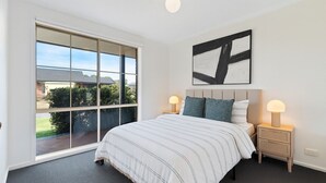 A bedroom with a large sliding glass door, a bed with striped bedding, two bedside tables with lamps, and a black and white abstract painting on the wall. - Family Oasis near Watergardens Parking (Sydenham)