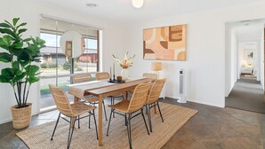 A dining area with a wooden table, wicker chairs, a vase with flowers, and a floor lamp. - Family Oasis near Watergardens Parking (Sydenham)