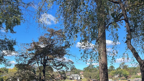 An outdoor seating area with Adirondack chairs and a table, overlooking a lake with boats and houses in the background. - NEW! Lake Front House,Private Dock,Kayaks,Beach (Troutman)