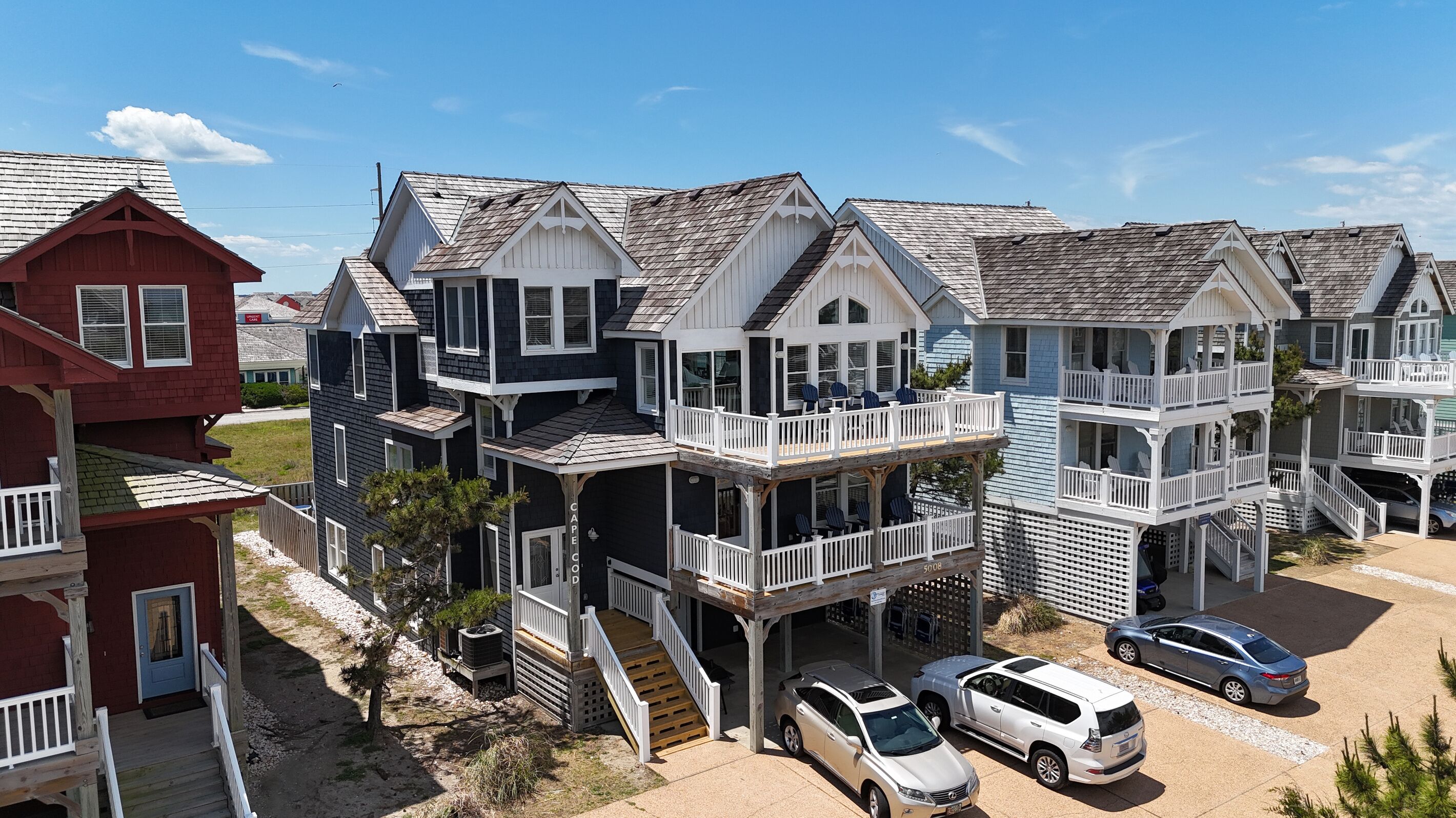 A beachfront property with multiple-story houses featuring balconies, a driveway with parked cars, and a clear sky.