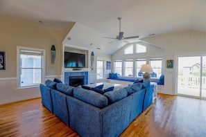 A living room with a sectional sofa, a fireplace, a television, and a large window.