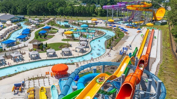 Un parc aquatique doté de nombreux toboggans et de plusieurs piscines, entouré d’espaces de détente et de parasols.