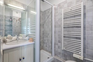 A bathroom with a glass shower enclosure, a white sink, and a towel rack.