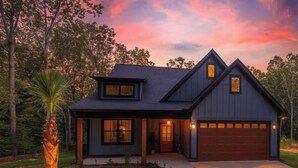 Uma casa moderna de dois andares com garagem, cercada por árvores e um gramado bem cuidado.
