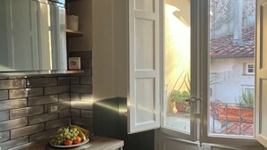 Une cuisine équipée d’un four encastré, avec un panier de fruits sur le plan de travail et une fenêtre donnant sur les bâtiments environnants.