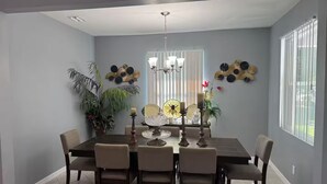A dining room with a dark wooden table, six chairs, a chandelier, and decorative wall art. - Cool 3-bedroom house with AC in the Sunshine State (Lehigh Acres)