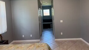 A hallway with grey walls, a tiled floor, and a door leading to another room. - Cool 3-bedroom house with AC in the Sunshine State (Lehigh Acres)