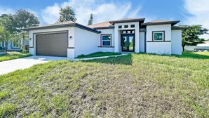 A modern two-story house with a garage, a front door, and a small porch. - Cool 3-bedroom house with AC in the Sunshine State (Lehigh Acres)