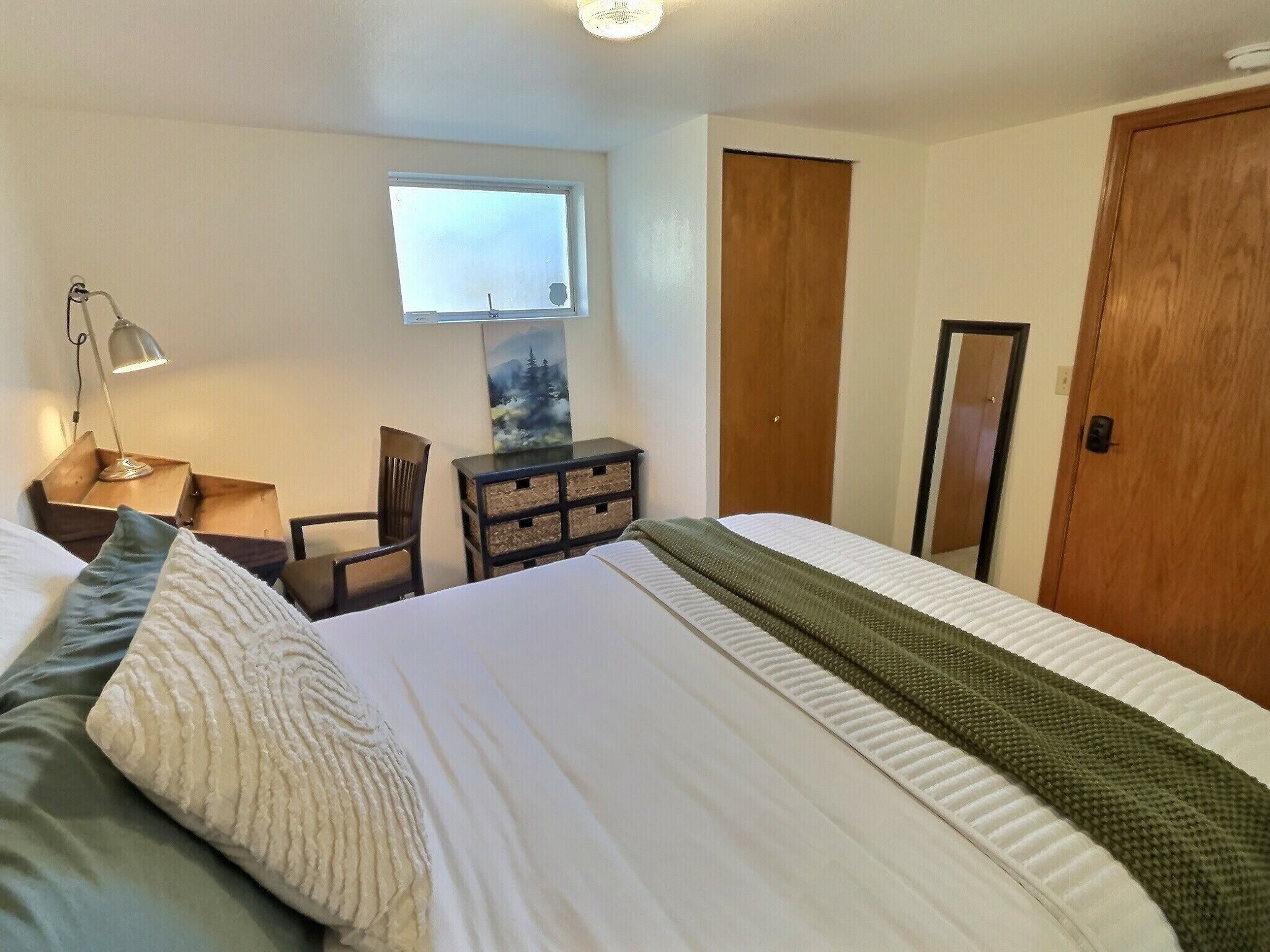 Ett hotellrum med en säng, ett skrivbord med en lampa, en stol, en byrå, en tavla, ett fönster och en dörr.