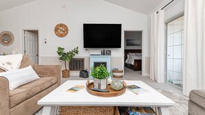 Un salon avec un canapé blanc, une table basse ornée d’une plante, un téléviseur à écran plat et une cheminée.