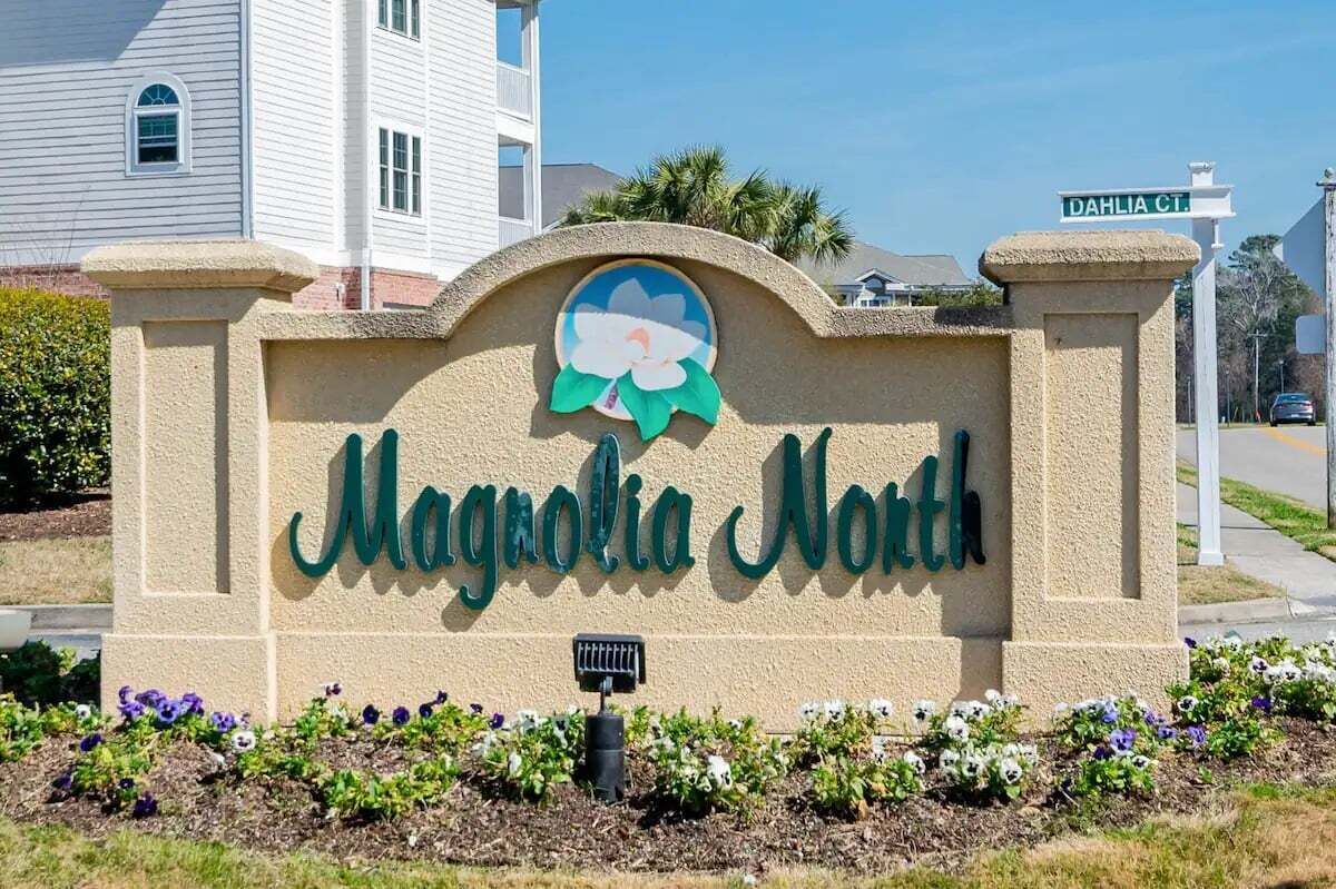 Señal de Magnolia North con un emblema floral, rodeada de un jardín ajardinado.