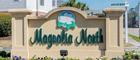 Señal de Magnolia North con un emblema floral, rodeada de un jardín ajardinado.