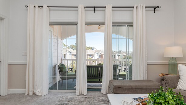 Un salon doté d’une grande porte-fenêtre coulissante donnant sur un balcon, d’un fauteuil vert, d’un canapé marron, d’une table basse blanche et d’une lampe.