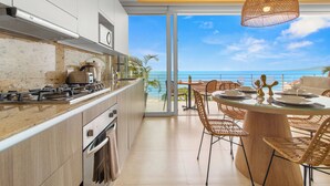 Cocina moderna con una isla grande, comedor con sillas de mimbre y vista al océano.