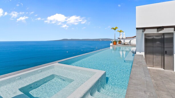 Una piscina con agua azul cristalina, un edificio blanco y vistas al océano.