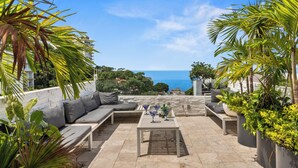 An outdoor patio with a sofa, table, and potted plants.