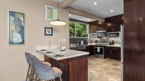 A modern kitchen with a central island, bar stools, wooden cabinets, and stainless steel appliances.