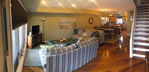 A living room with a striped sofa, a glass coffee table, and a television on a cabinet. - Beach Block condo, 2 bed, 2.5 bath - Perfect for couples or small families! (Brigantine)