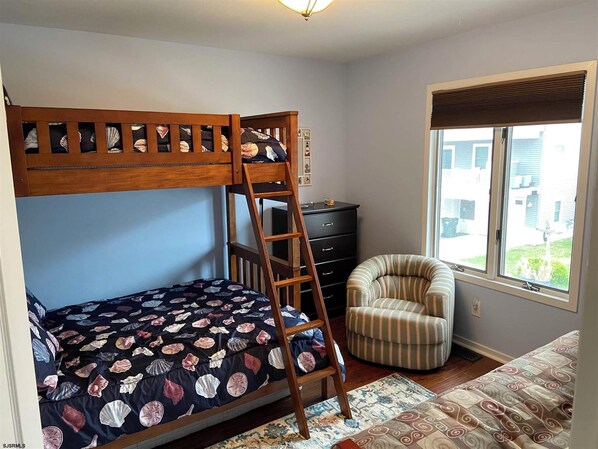 A bedroom with a bunk bed, a chair, a dresser, and a window with blinds.
