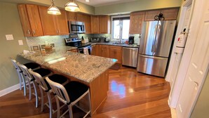 A modern kitchen with wooden cabinets, stainless steel appliances, and a granite island with bar stools. - Beach Block condo, 2 bed, 2.5 bath - Perfect for couples or small families! (Brigantine)