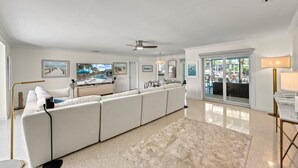 A spacious living room with a large white sectional sofa, a ceiling fan, and a view of a pool through the glass doors. - Siesta Key Waterfront Oasis - Heated Pool, Dock, Walk to Village & Beach (Siesta Key)