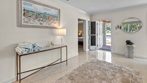 A hallway with a marble floor, a console table with towels, a framed painting, a lamp, and a mirror. - Siesta Key Waterfront Oasis - Heated Pool, Dock, Walk to Village & Beach (Siesta Key)