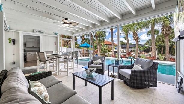 A spacious patio with a pool, outdoor seating, and a kitchen area visible through large windows. - Siesta Key Waterfront Oasis - Heated Pool, Dock, Walk to Village & Beach (Siesta Key)