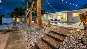 A backyard with a pool, palm trees, string lights, and a wooden deck. - Siesta Key Waterfront Oasis - Heated Pool, Dock, Walk to Village & Beach (Siesta Key)