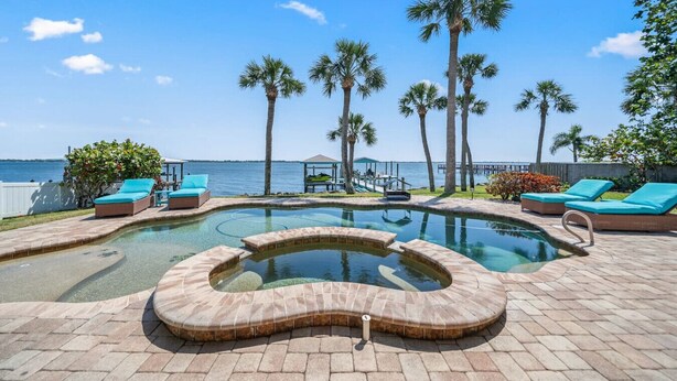 A pool area with lounge chairs and palm trees, overlooking a body of water.