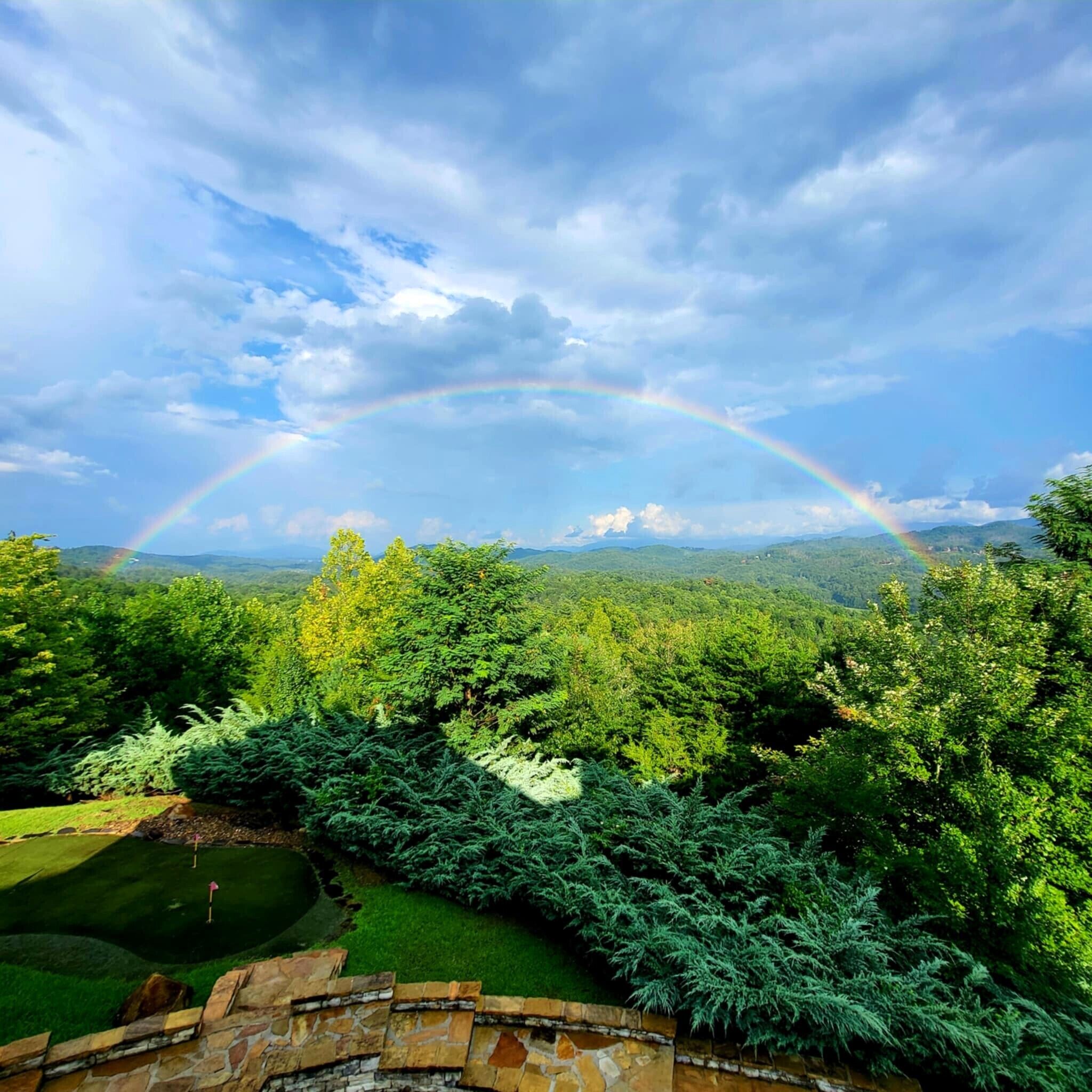 A lush landscape with a stone wall and a view of a golf course.