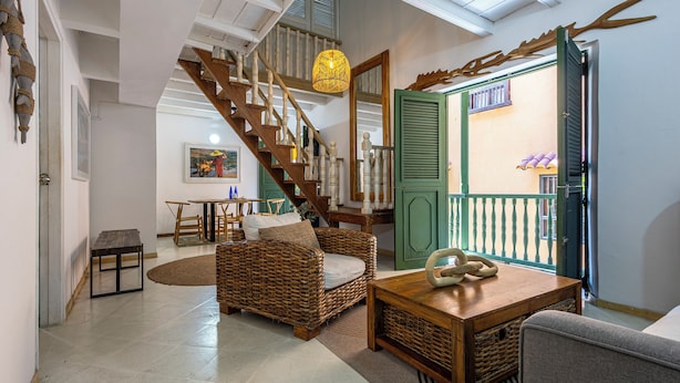 A spacious living area with a wooden staircase, wicker furniture, and a view through an open door.