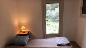 A small room with two beds, a nightstand with a lamp, and a door leading to a garden. - La Téolière (countryside and private pool) (FIGANIERES)