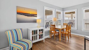 A dining area with a table and chairs, a white cabinet with books, and a painting on the wall. - Tee Off by Brunswick Vacation Rentals: 6 Bedrooms with Amazing Views & Pool! (Ocean Isle Beach)