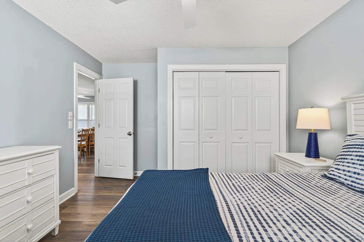 A bedroom with a bed, a dresser, a nightstand with a lamp, and a closet.