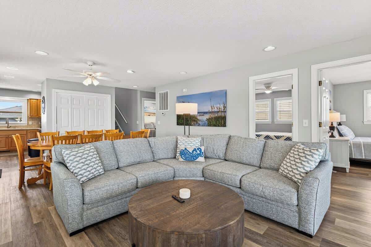 A living room with a sectional sofa, a round coffee table, and a dining area with wooden chairs.