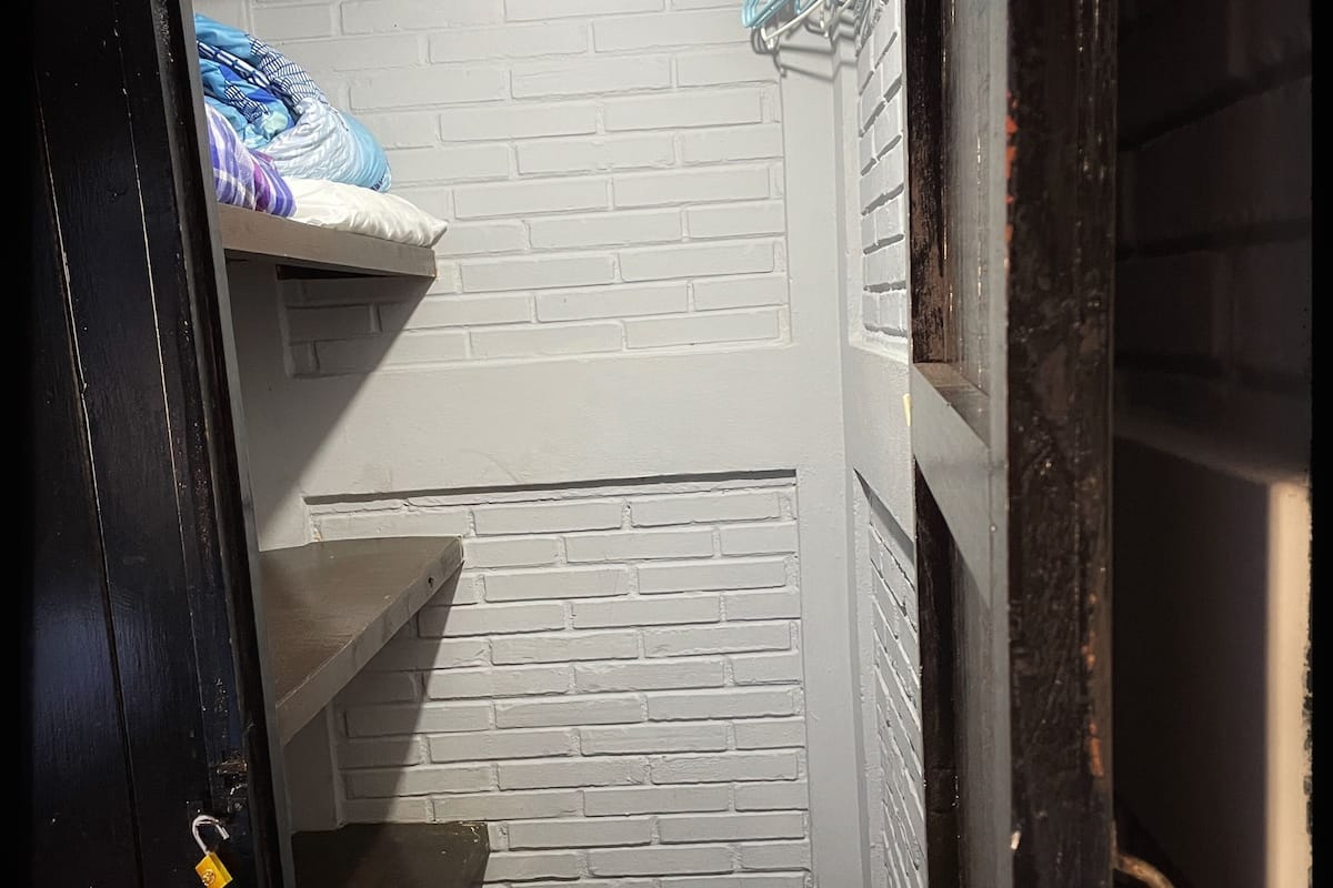 A narrow hallway with white brick walls, a wooden door, and a metal rod with clothes hangers.