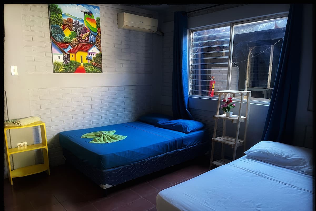 A room with a bed, a small table, a window with a view, and a wall with a colorful painting.
